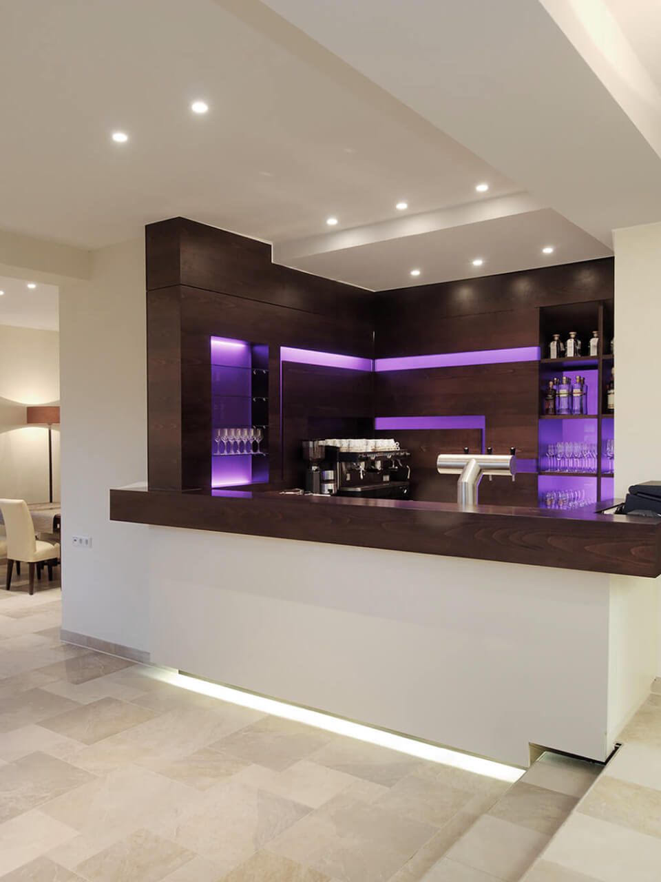 Moderne Bar in dunkler Holzoptik mit LED-Beleuchtung und diversen Flaschen und Gläsern.