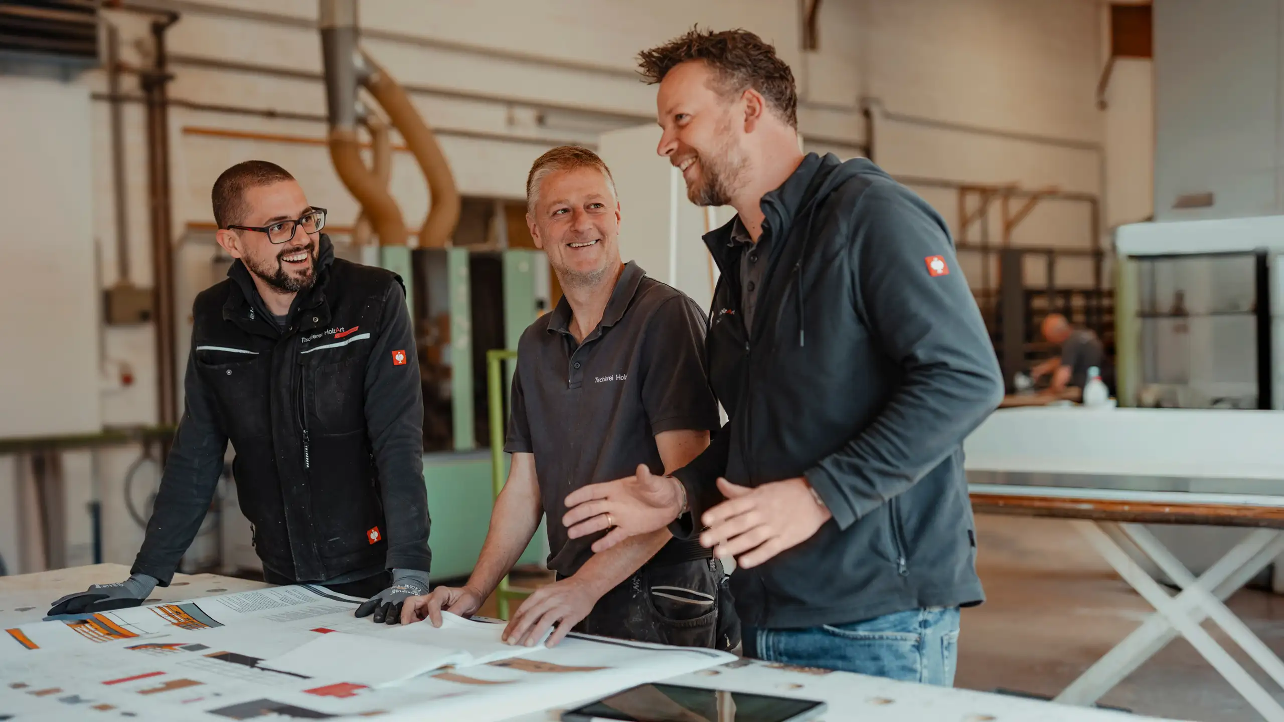 Das Team der Tischlerei HolzArt bespricht sich zu einem Projekt an einem Tisch mit Plänen auf Papier.